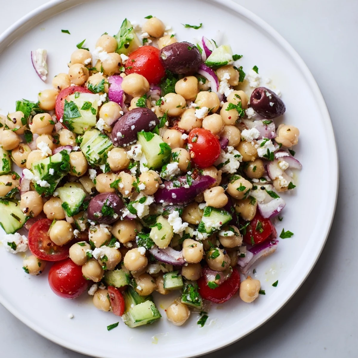 A bowl of Mediterranean Chickpea Salad showcases juicy cherry tomatoes, cucumbers, Kalamata olives, and creamy feta cheese tossed in a bright lemon dressing.