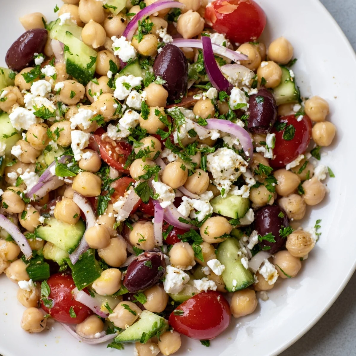 Bright Mediterranean Chickpea Salad features crisp vegetables, briny olives, and crumbled feta cheese, garnished with parsley and tossed in a lemon vinaigrette.