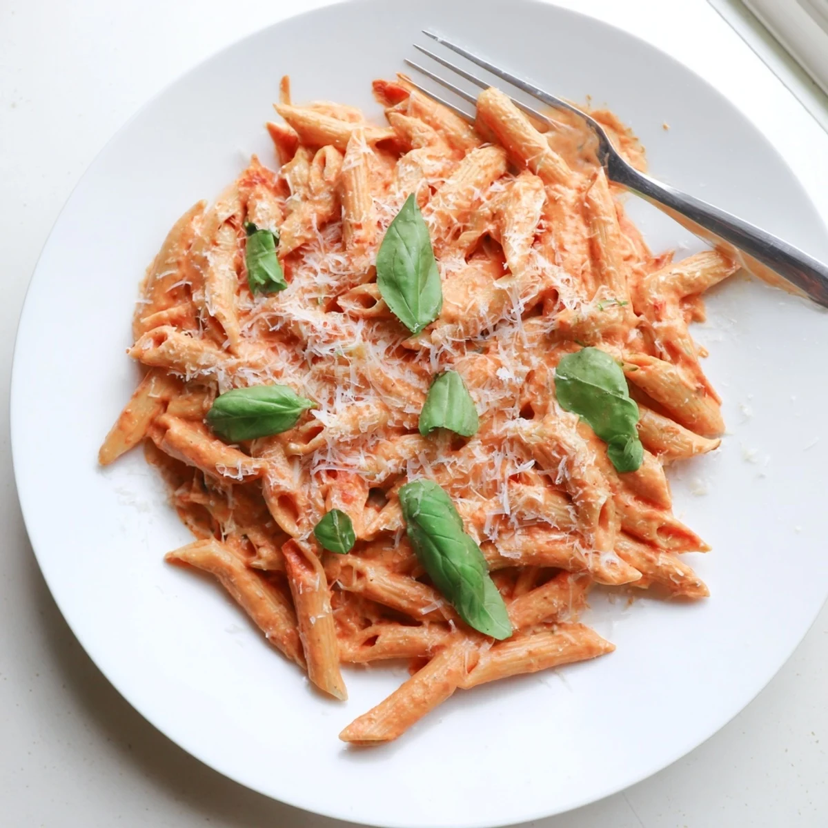 A close-up of penne pasta coated in a rich, velvety tomato cream sauce, with steam rising and garlic visible.