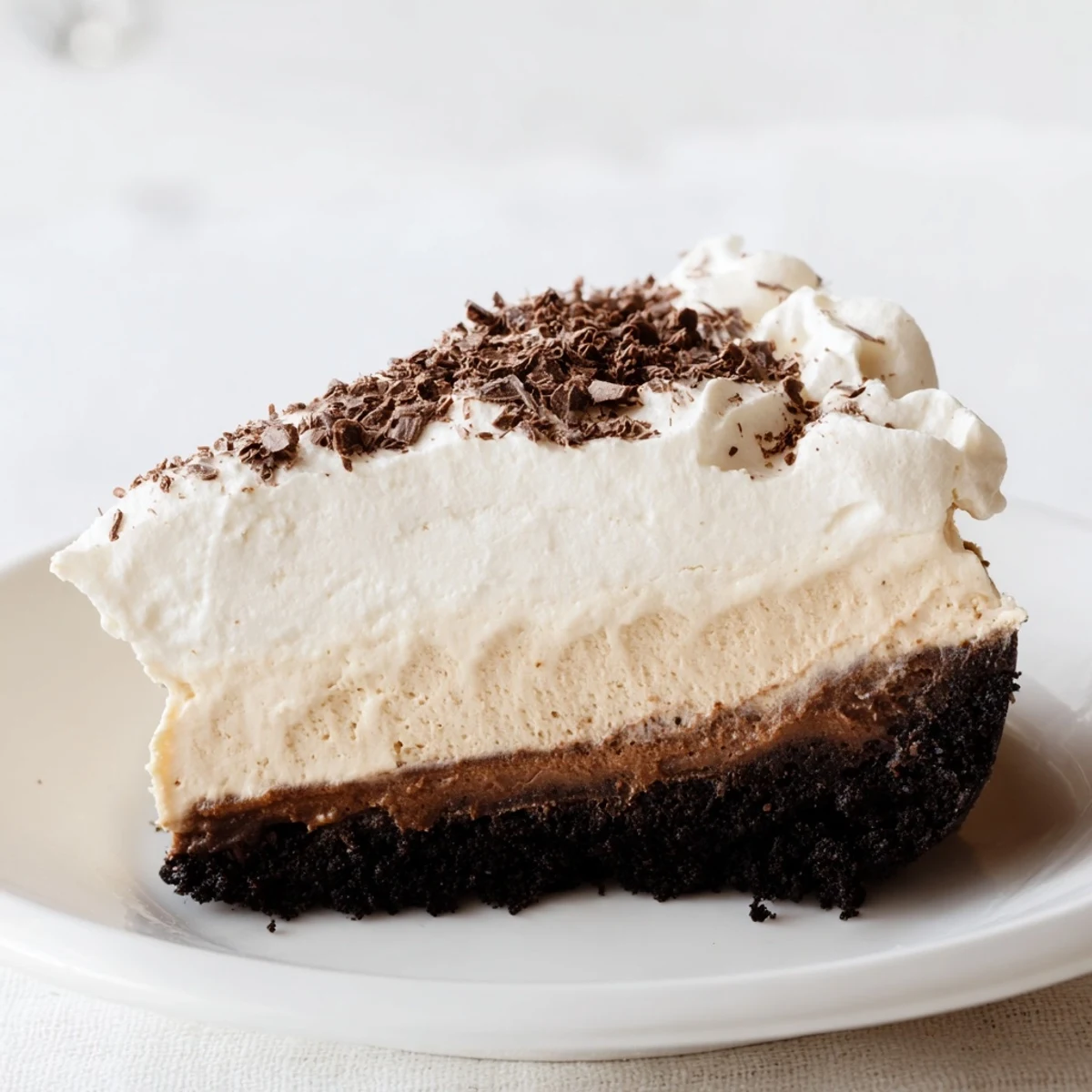 A slice of Bailey Style Irish Cream Cheesecake on a white plate, topped with a cloud of whipped cream and a sprinkle of cocoa powder.  