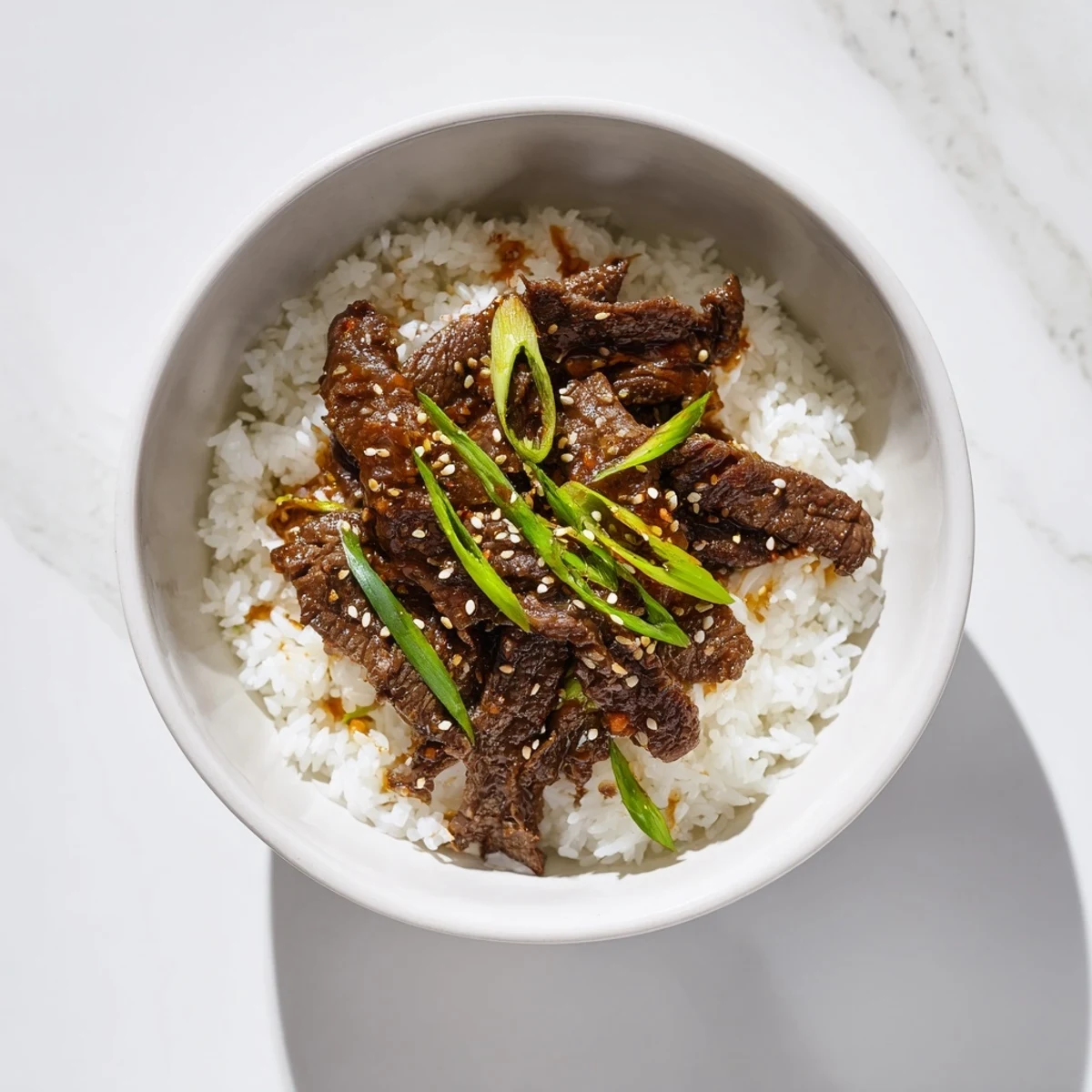 Steaming bowl of homemade Spicy Korean Beef Bowl garnished with scallions and sesame, paired with kimchi for a tangy kick.