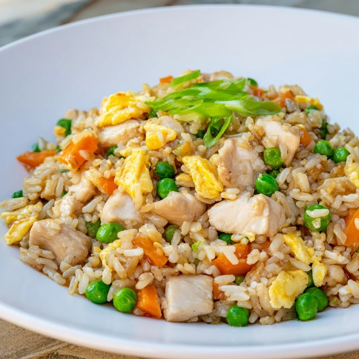 Steaming bowl of homemade Chicken Fried Rice with Peas and Carrots, garnished with sliced green onions and ready to serve for a quick weeknight dinner.