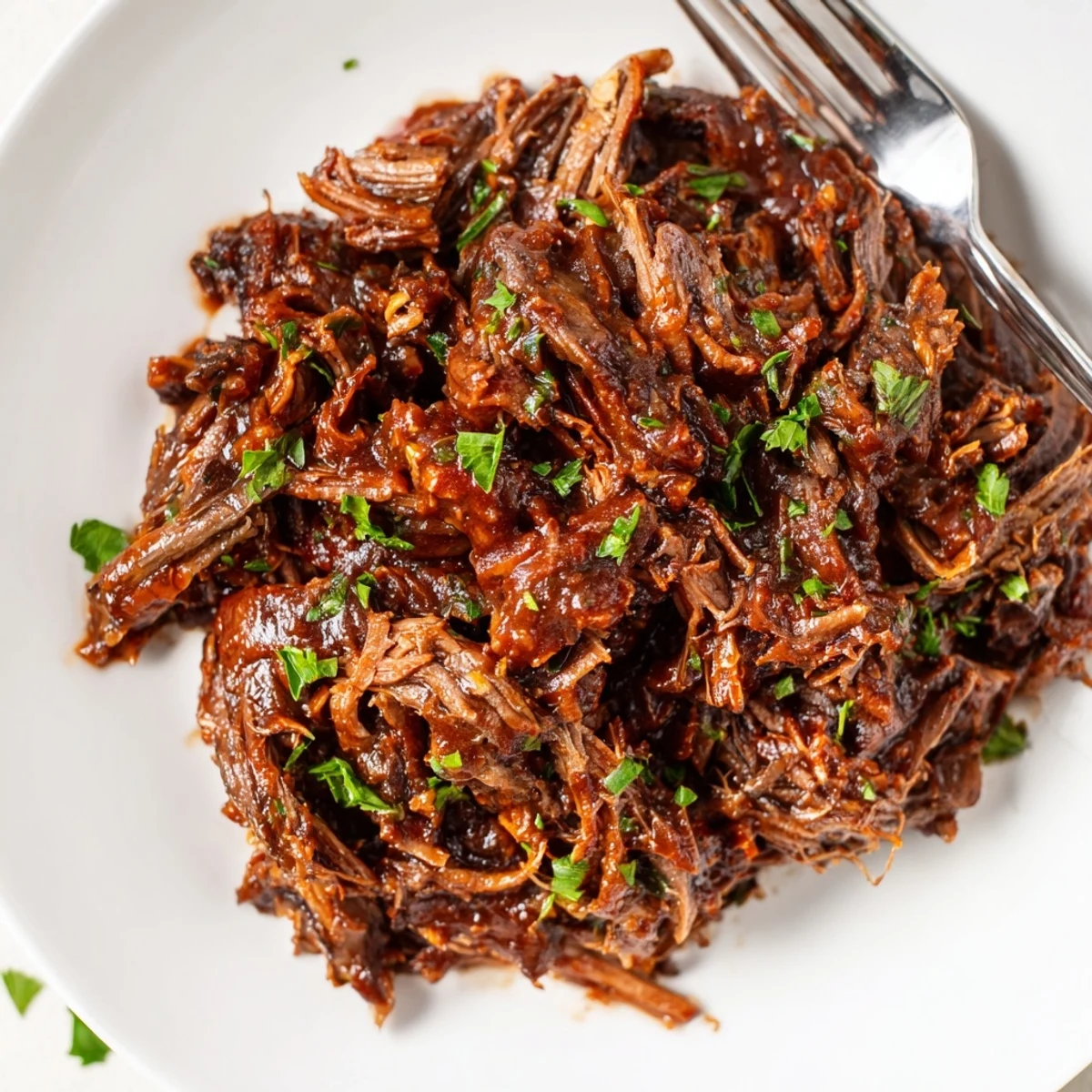 A slice of tender slow cooker beef brisket glistening with rich, smoky BBQ sauce, served on a soft roll with chopped parsley.