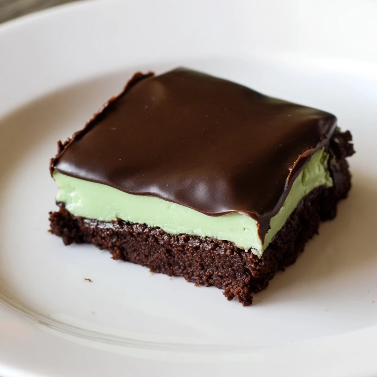 Sharp knife slices show the green mint cream layer inside Shamrock Mint Brownies with Chocolate Ganache, plated for a St. Patrick's Day party.