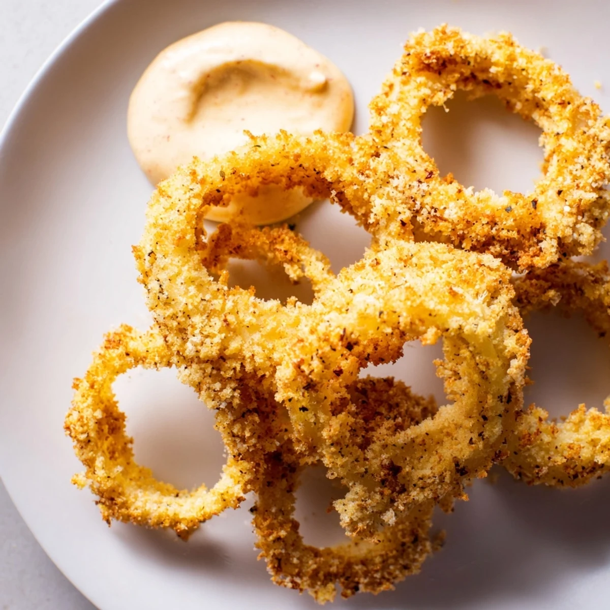 Serving of Crispy Air Fryer Onion Rings with Chipotle Mayo alongside a burger for a complete meal.