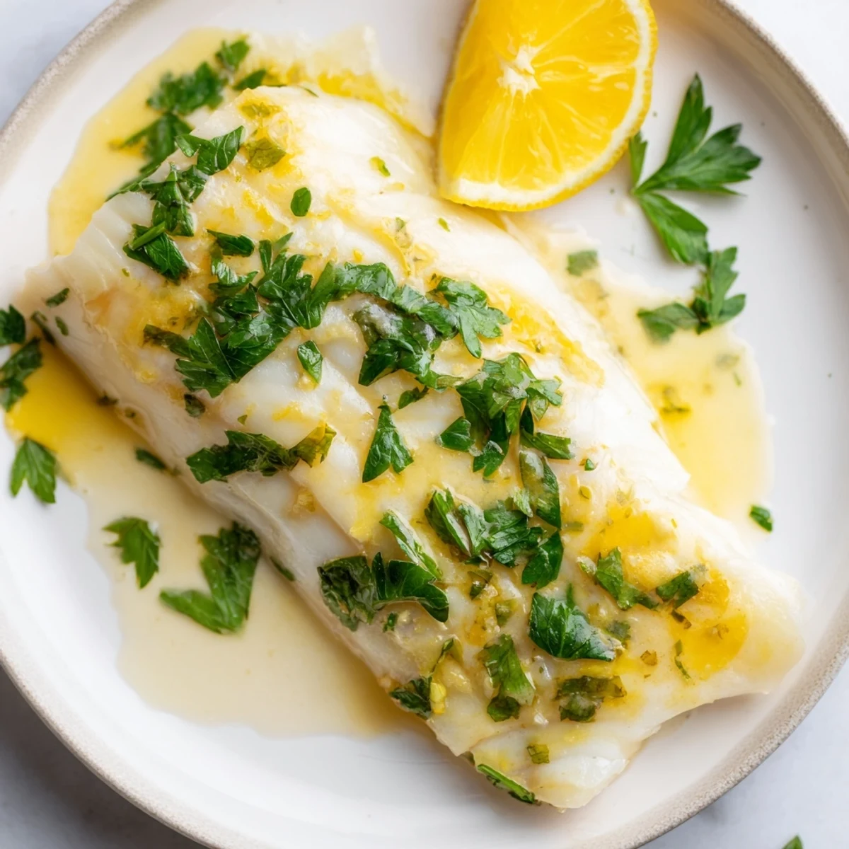 Golden brown Baked Halibut with Lemon Butter topped with fresh parsley and lemon wedges, served on a rustic board. 
