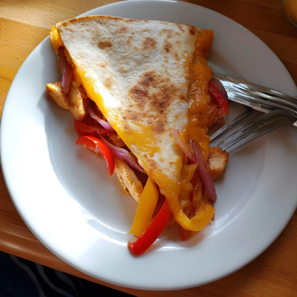 Golden-brown Chicken Quesadillas with Peppers are sliced into wedges, revealing melted cheddar and mozzarella and colorful peppers on a plate.