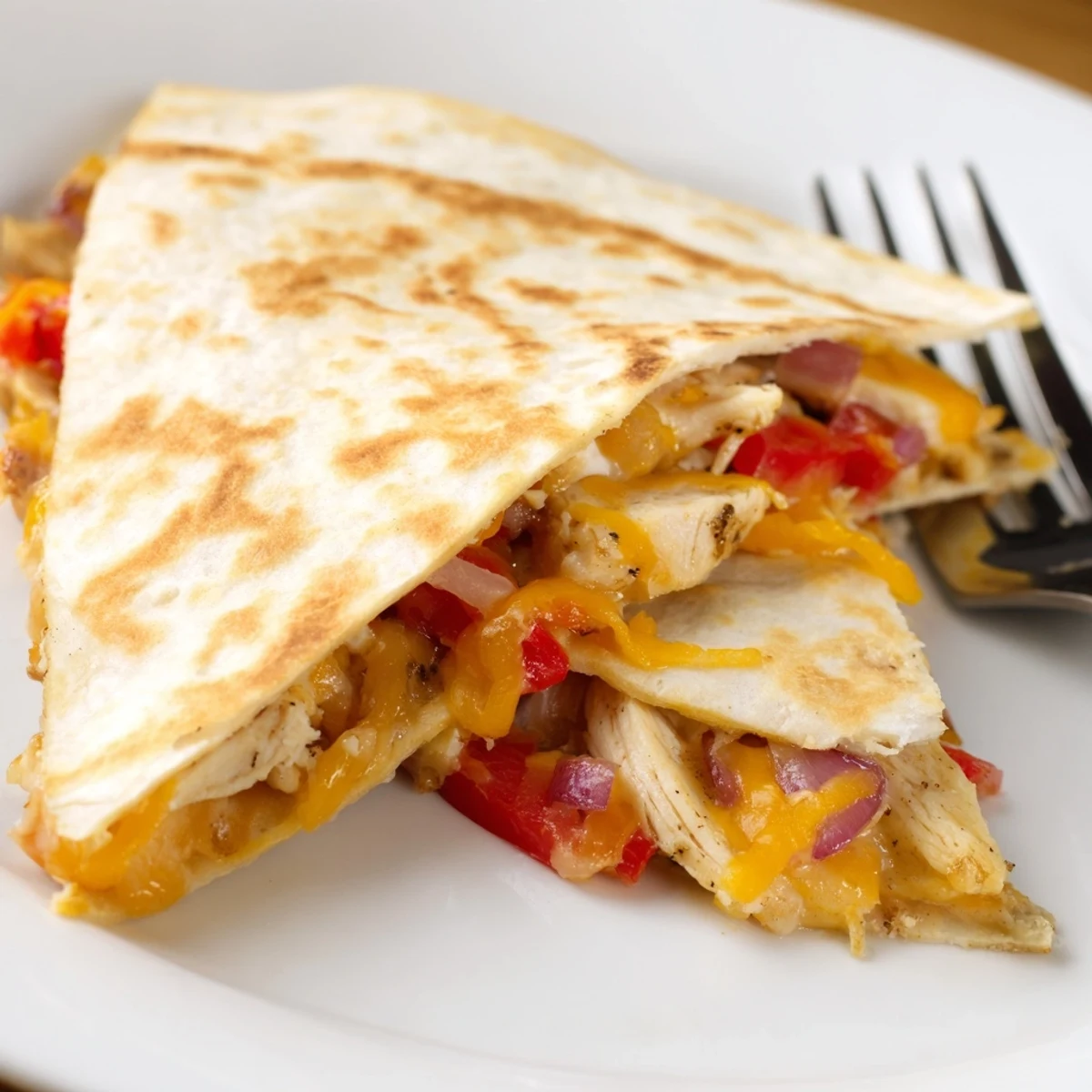 A close-up shows one slice of Chicken Quesadillas with Peppers being lifted, revealing melted cheese and savory chicken filling.