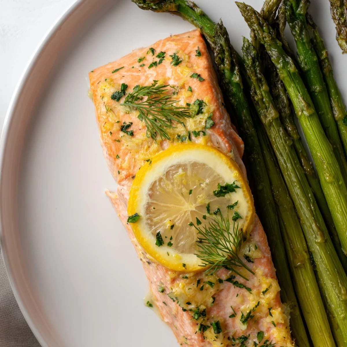Four baked salmon fillets glisten with lemon and herbs beside tender asparagus on a sheet pan, perfect for serving with wild rice.