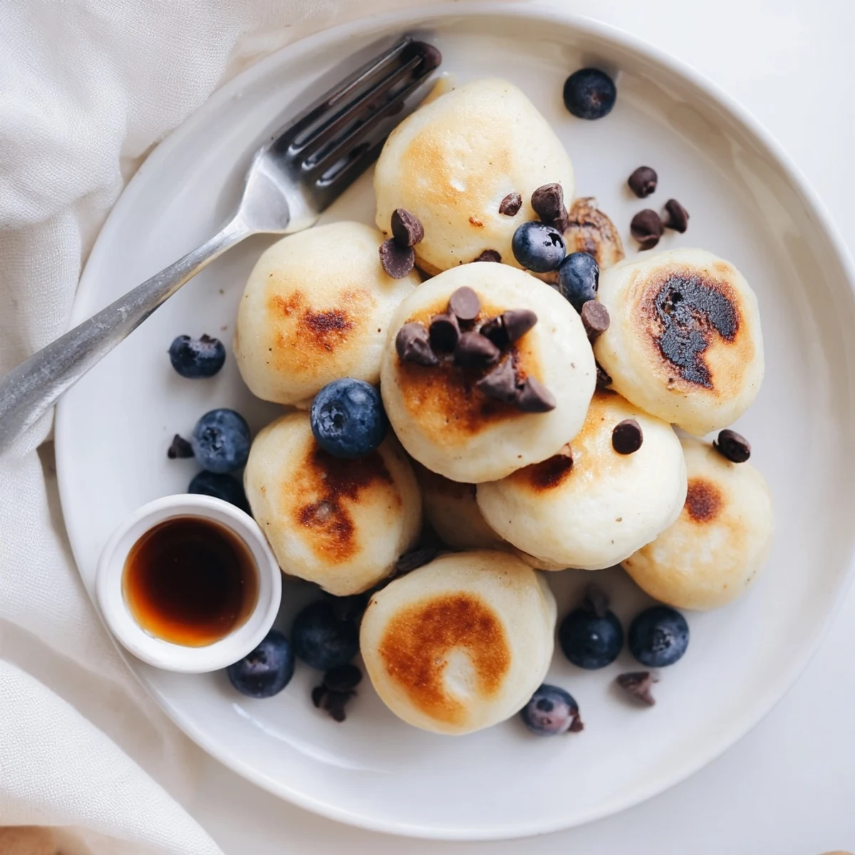 Stack of warm Pancake Poppers topped with a pat of butter and a dusting of powdered sugar on a brunch plate.