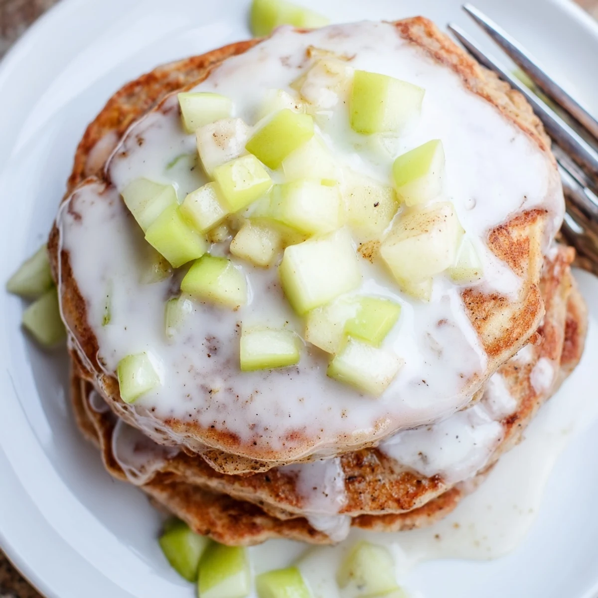 A close-up of glazed Apple Fritter Pancakes stacked high, drizzled with sweet vanilla glaze on a cozy breakfast plate.