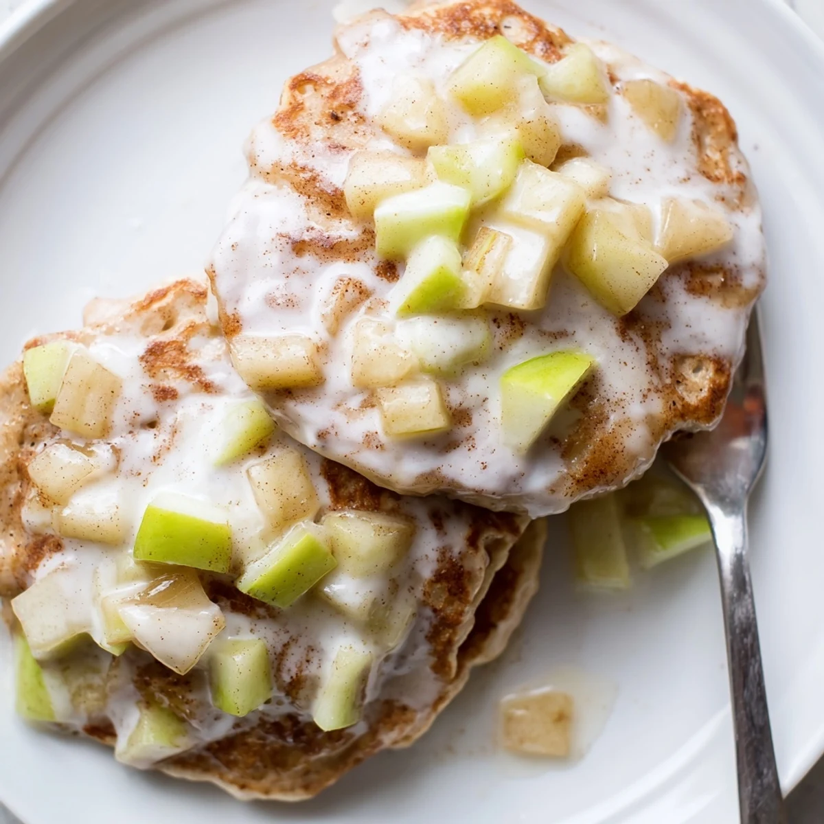A fluffy plate of Apple Fritter Pancakes topped with warm glaze, ready to be served with a steaming cup of coffee.