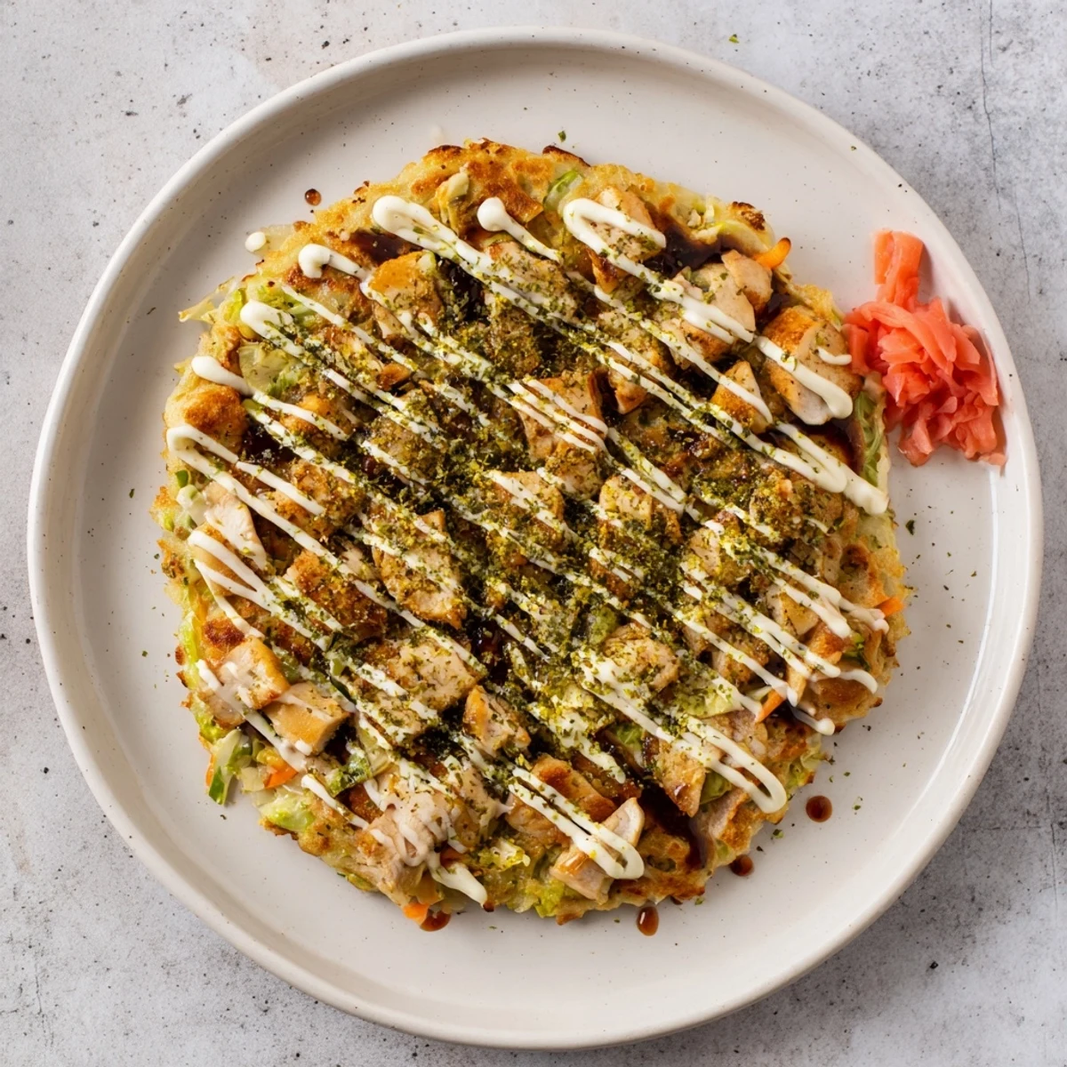 Savory Chicken Okonomiyaki with tender shredded cabbage and carrots, drizzled with tangy sauce and bonito flakes.