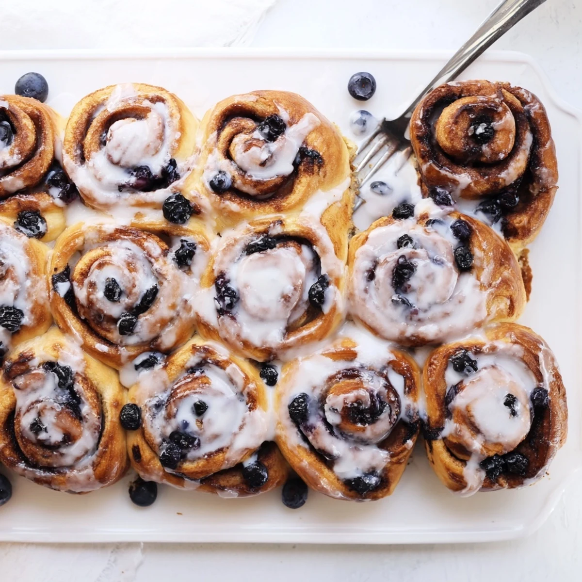 Golden-brown Blueberry Cinnamon Rolls fresh from the oven, drizzled with creamy vanilla glaze on a rustic wooden table.