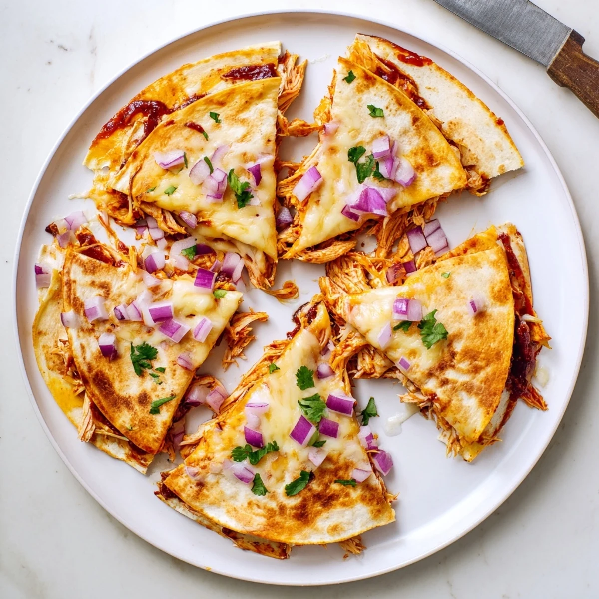 Freshly cooked hot honey BBQ chicken quesadillas rest on a plate, garnished with cilantro and red onion.