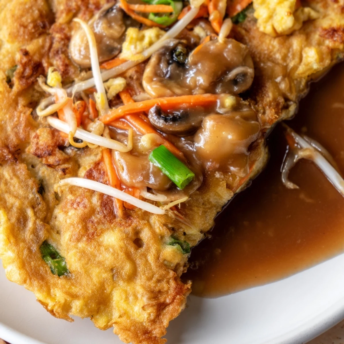 Golden brown crispy Egg Foo Young patties topped with savory brown gravy on white plate