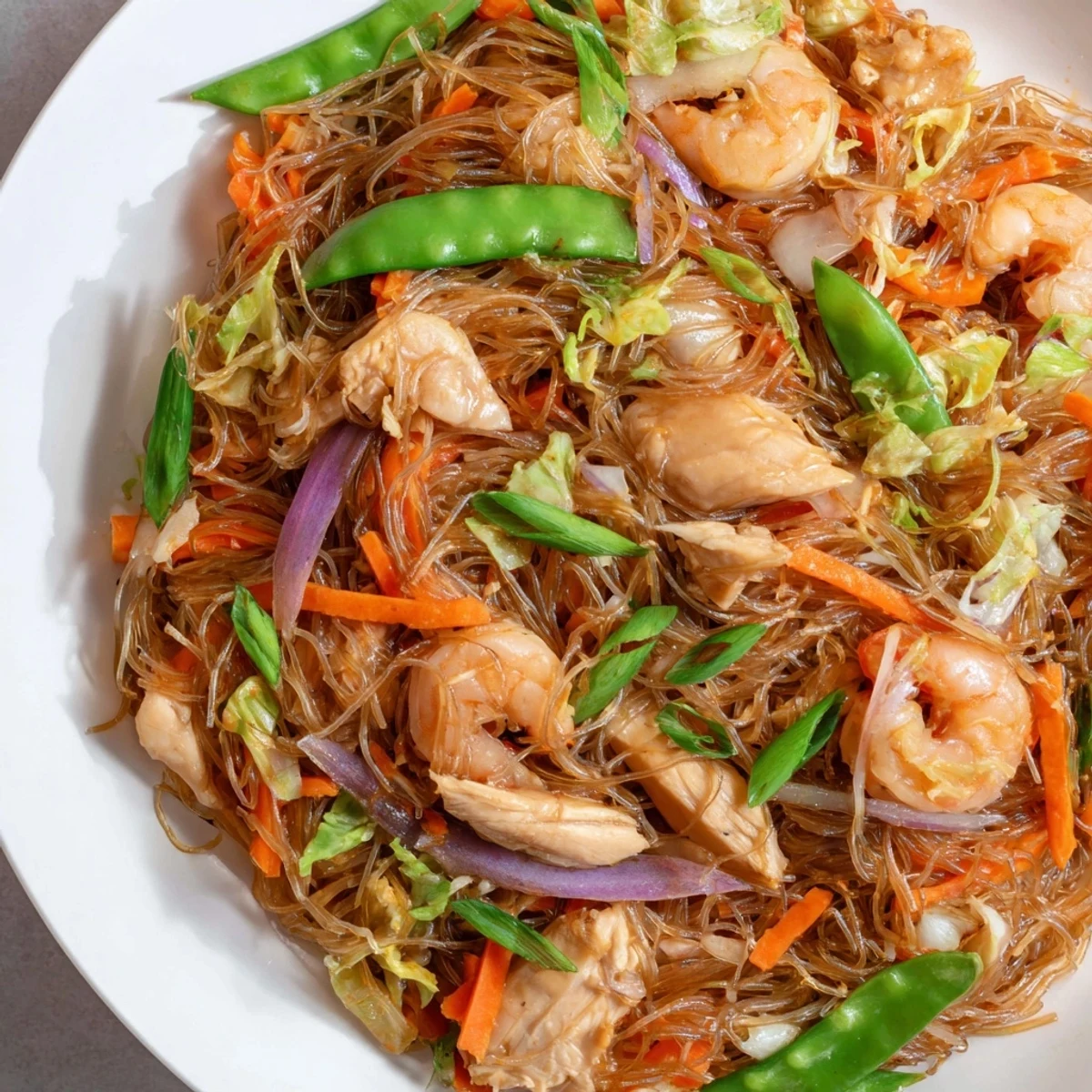 Steaming plate of traditional Pancit Bihon garnished with fresh scallions and served with bright calamansi wedges