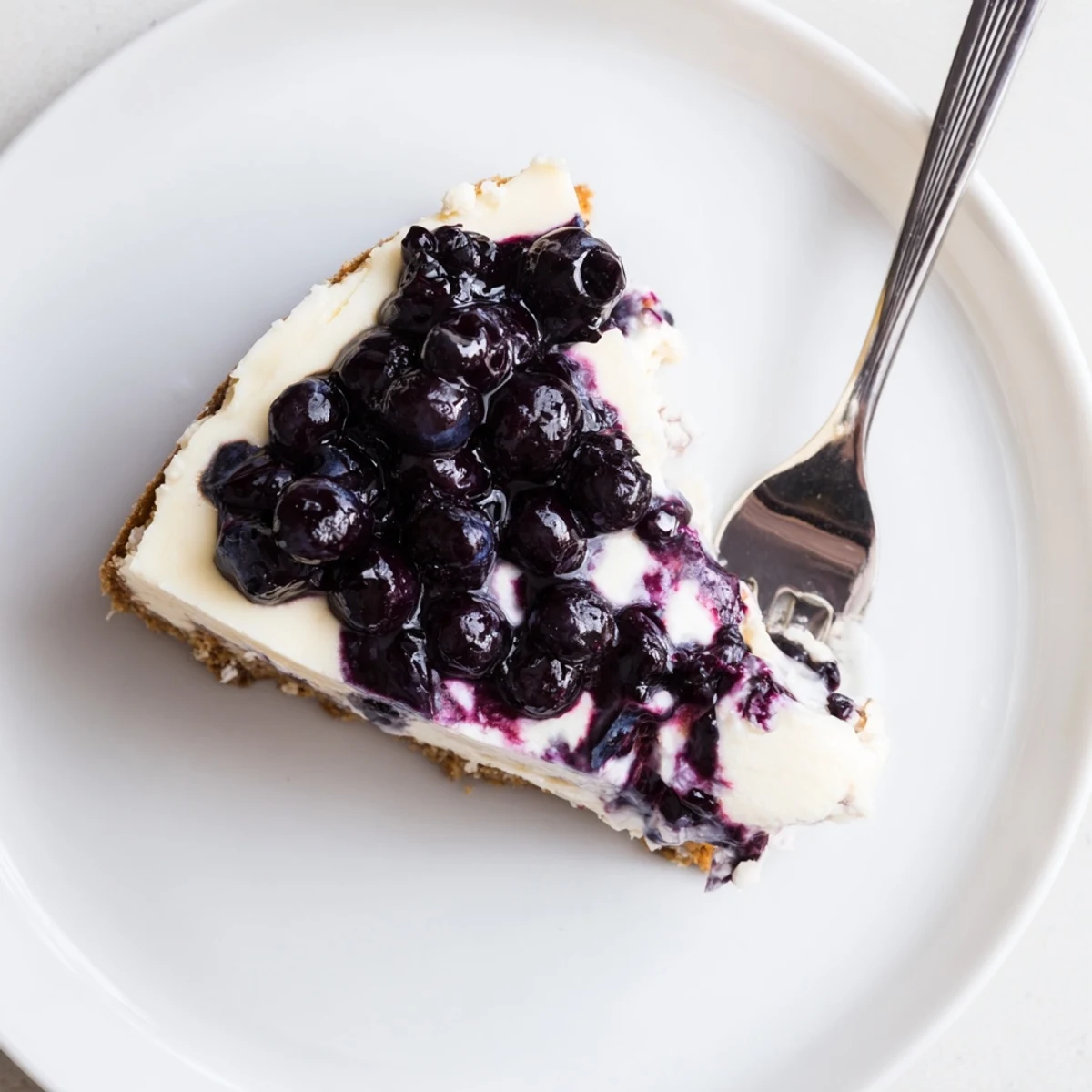 Rich blueberry cheesecake served on white plate with buttery graham cracker crust and fresh berry swirl