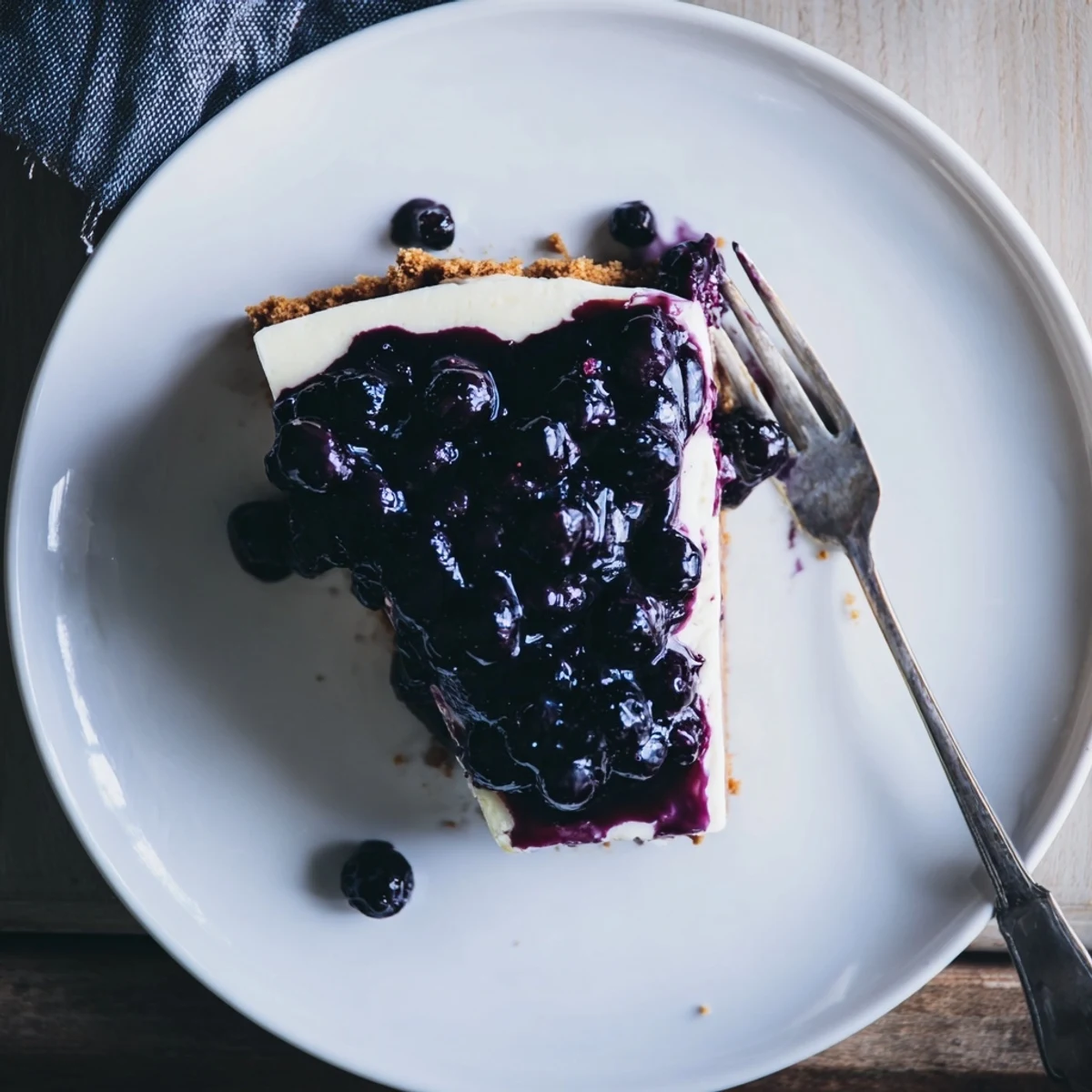 Creamy blueberry cheesecake slice featuring smooth vanilla filling topped with glossy purple blueberry compote