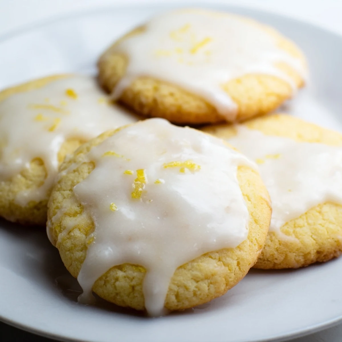 Golden lemon frosted cookies drizzled with tangy white glaze on a white serving plate