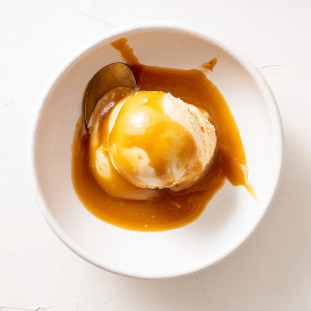Silky smooth easy caramel sauce pooled in a glass jar with a wooden spoon