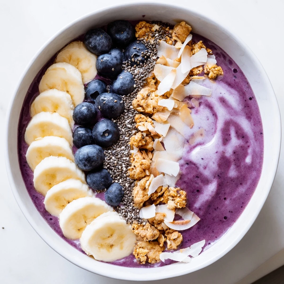 Thick blueberry smoothie bowl with Greek yogurt layered with colorful toppings and sliced fresh fruit