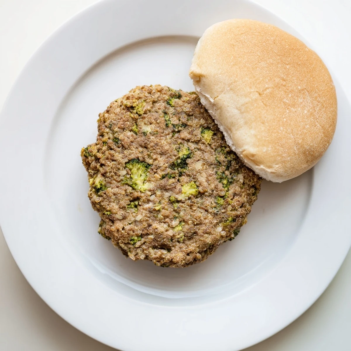 Golden pan-fried turkey broccoli and quinoa burgers served on a white plate with fresh green onions