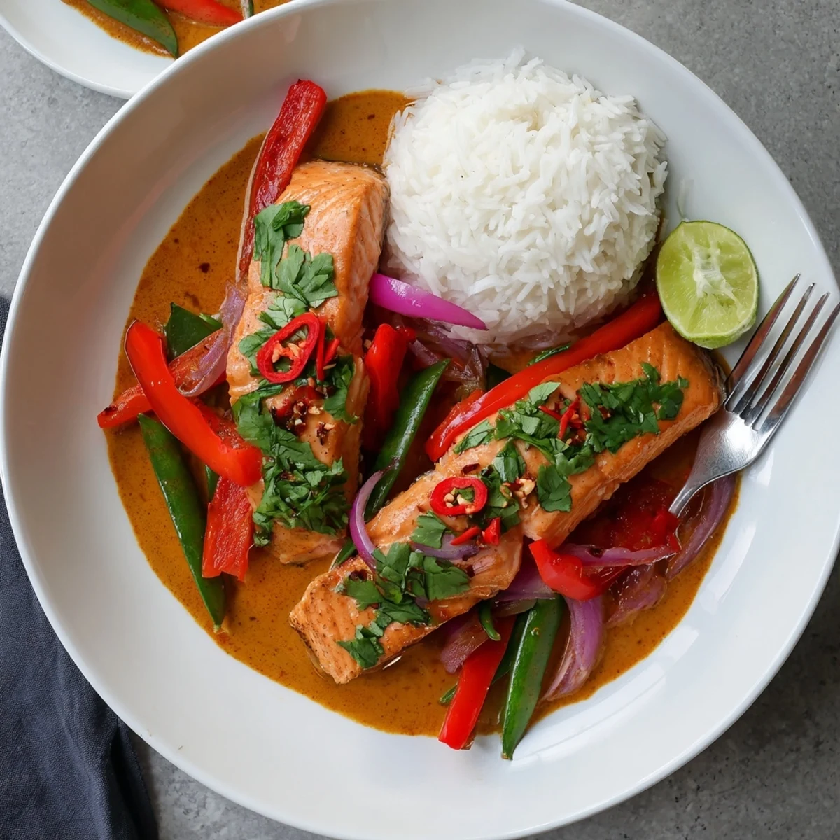 Steamy red curry coconut salmon plated over fluffy jasmine rice with crisp vegetables and herb garnish