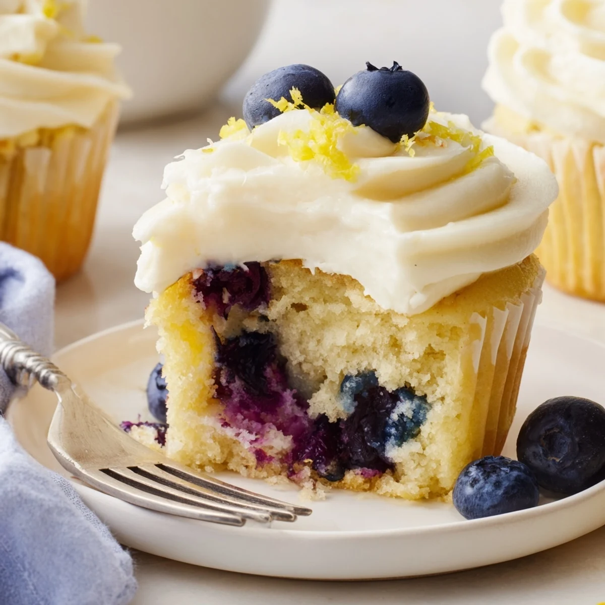 Freshly baked lemon blueberry cupcakes with swirls of lemon cream cheese frosting and zesty lemon zest