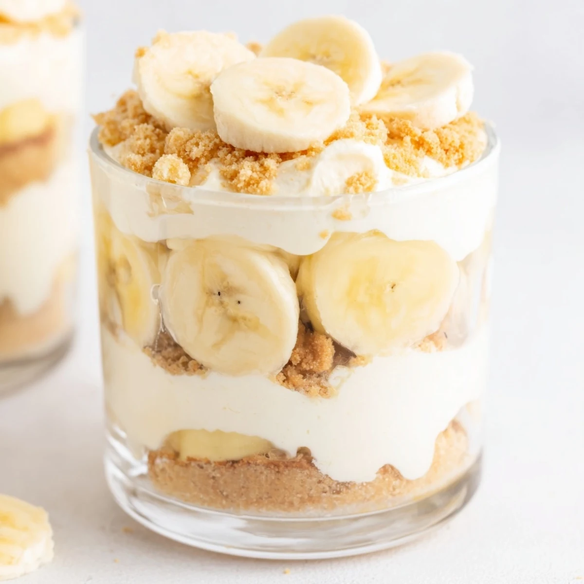 No bake banana pudding cheesecake cups topped with golden cookie crumbs and sliced bananas