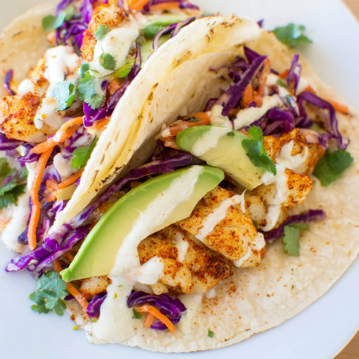 Golden tilapia fish tacos in warm tortillas with fresh avocado slices and tangy drizzle