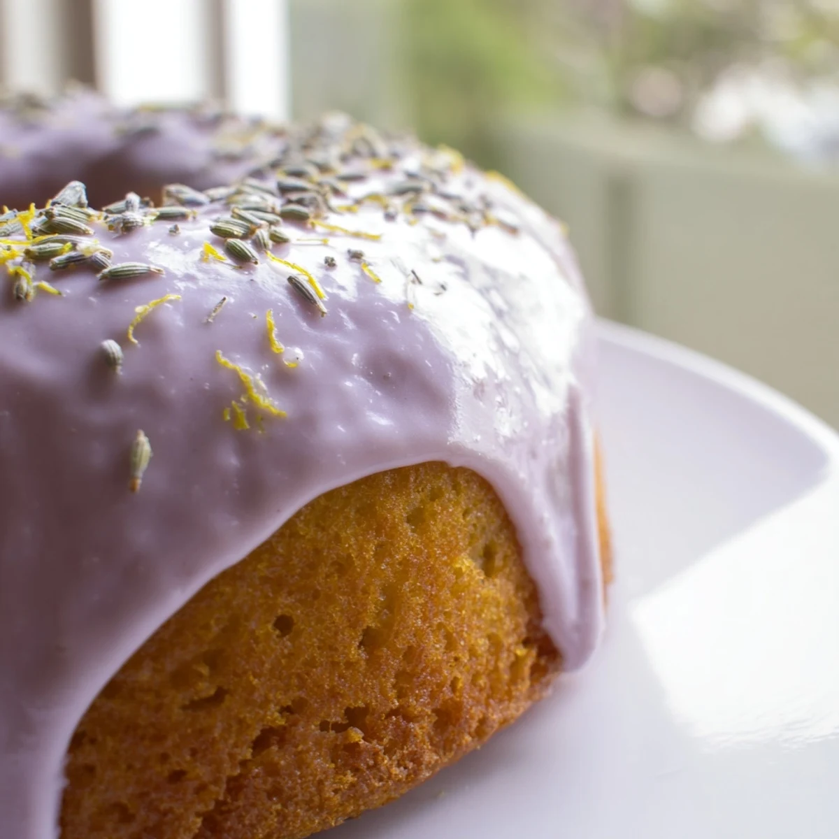 A plate of mini lemon cakes with lavender glaze set beside a tea cup