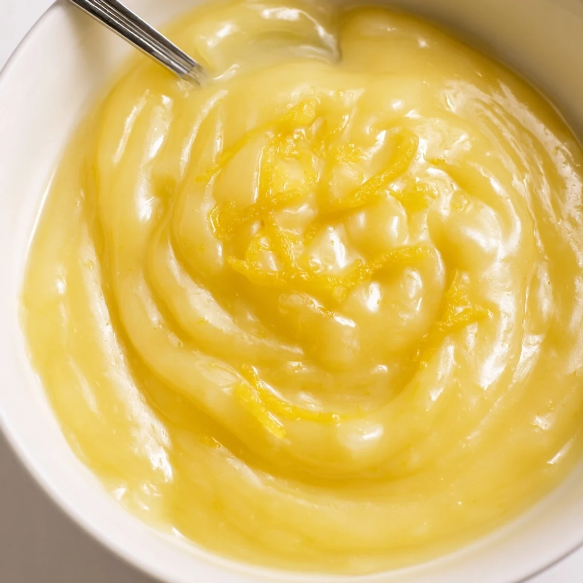 Lemon Curd Recipe: glossy, sunlit yellow curd spooned into glass jar.