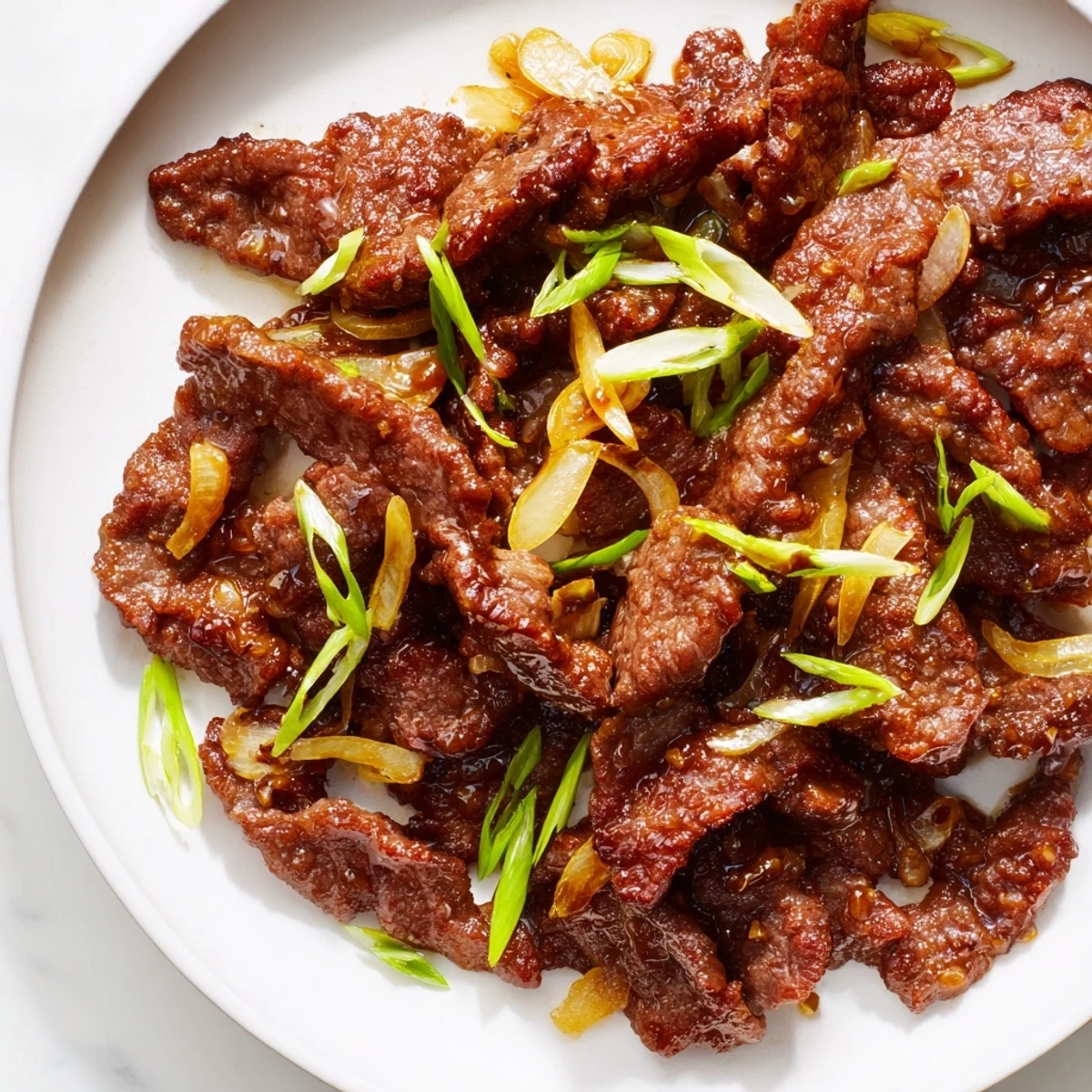 Sizzling skillet of crispy beef and onion stir fry garnished with fresh green spring onions