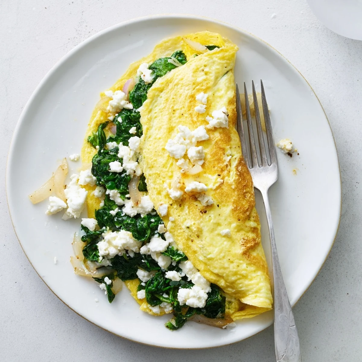 Golden folded spinach feta omelet sprinkled with creamy crumbles on a white plate