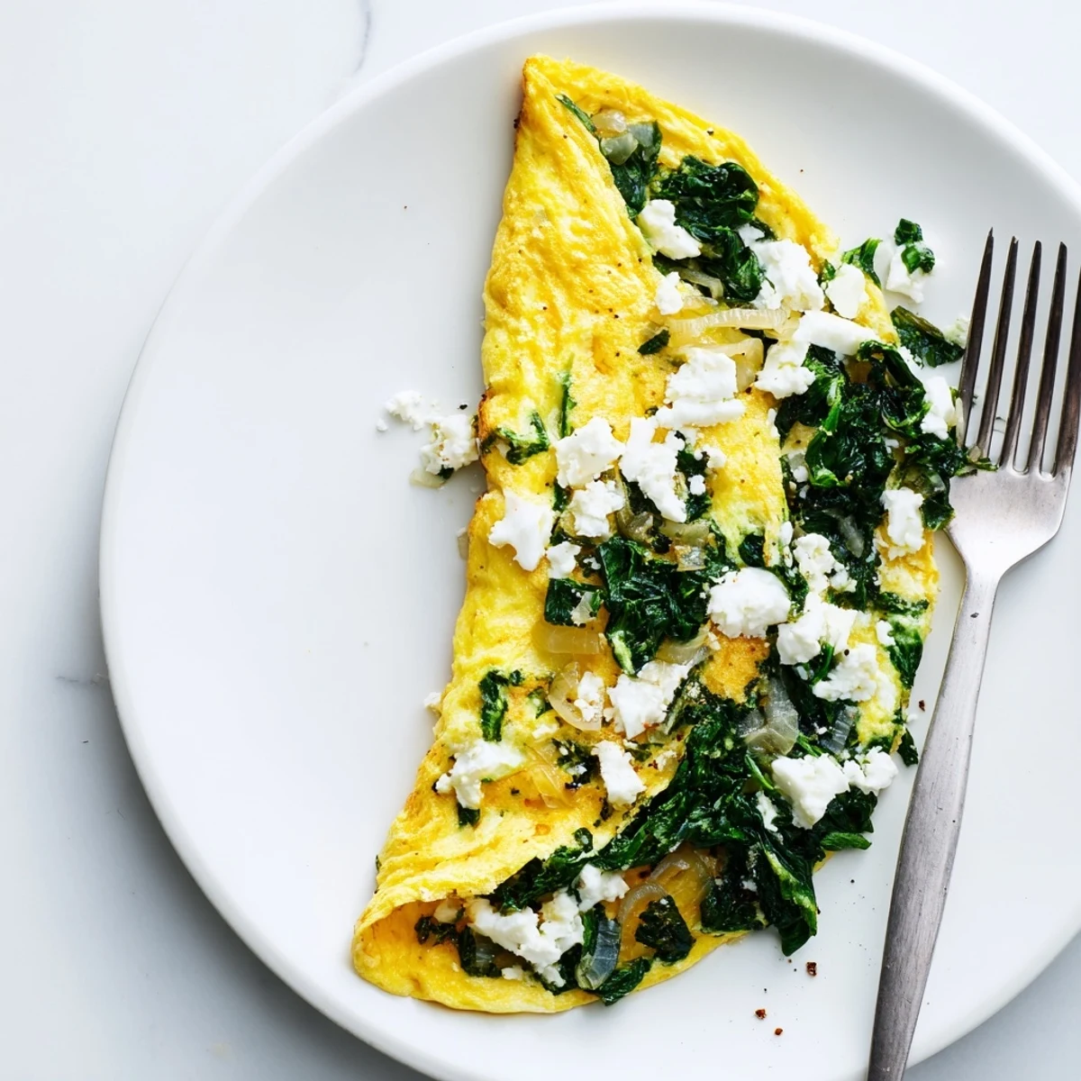 Savory breakfast spinach feta omelet folded around fresh spinach and salty crumbled cheese