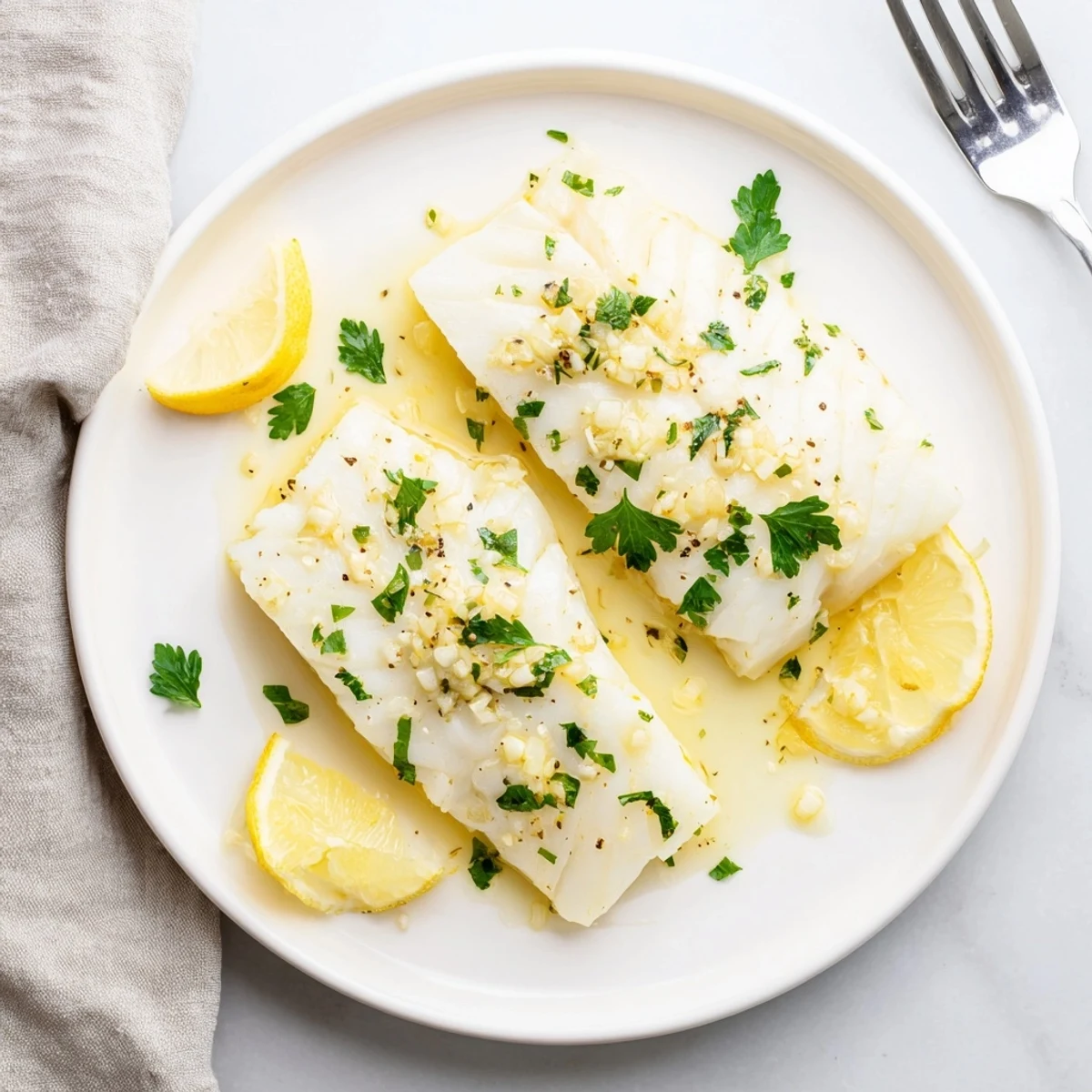 Flaky white fish topped with melted garlic butter and bright lemon zest on a white plate