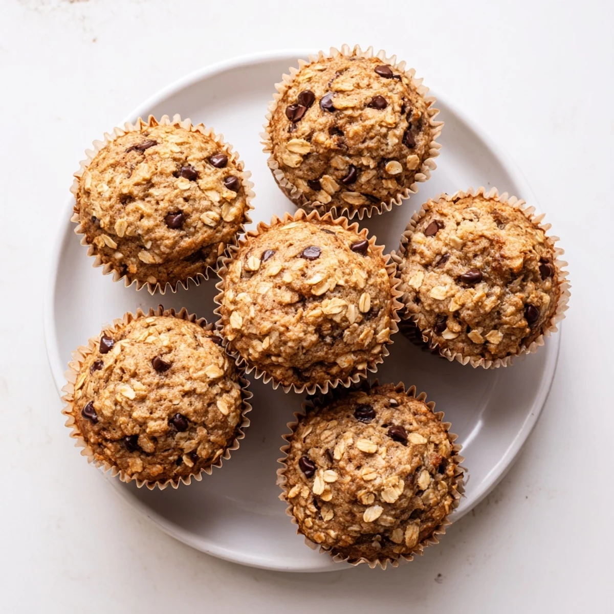 Golden banana chocolate chip muffins with oats cooling on a wire rack with melty chocolate chips visible on top