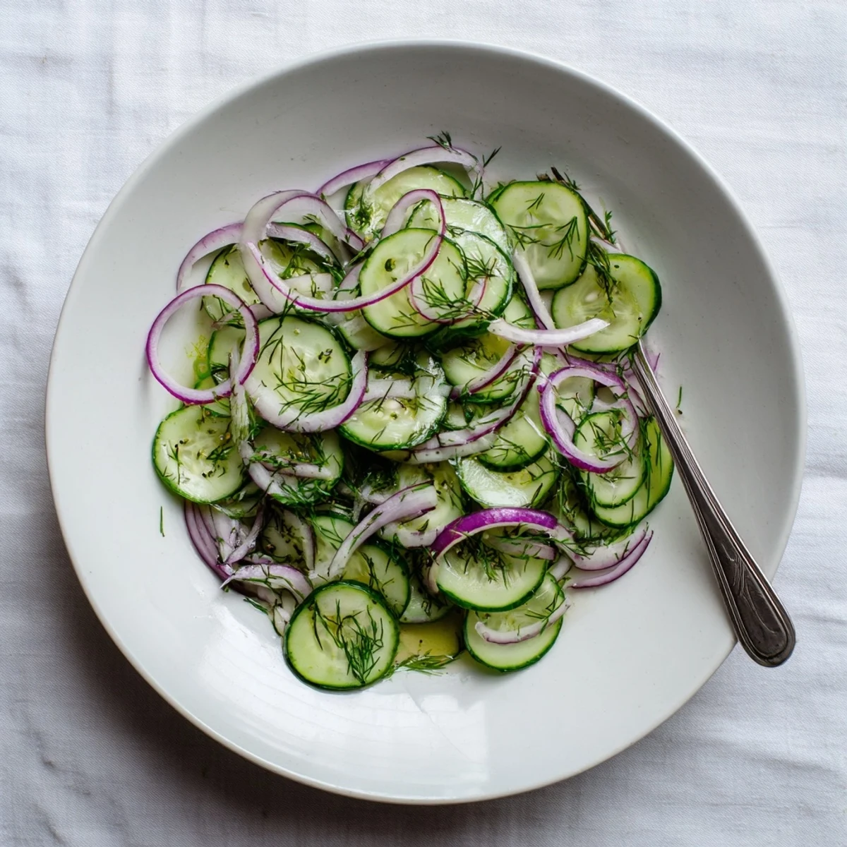 Crisp refreshing cucumber salad plated in white bowl with vibrant red onion ribbons and green herbs