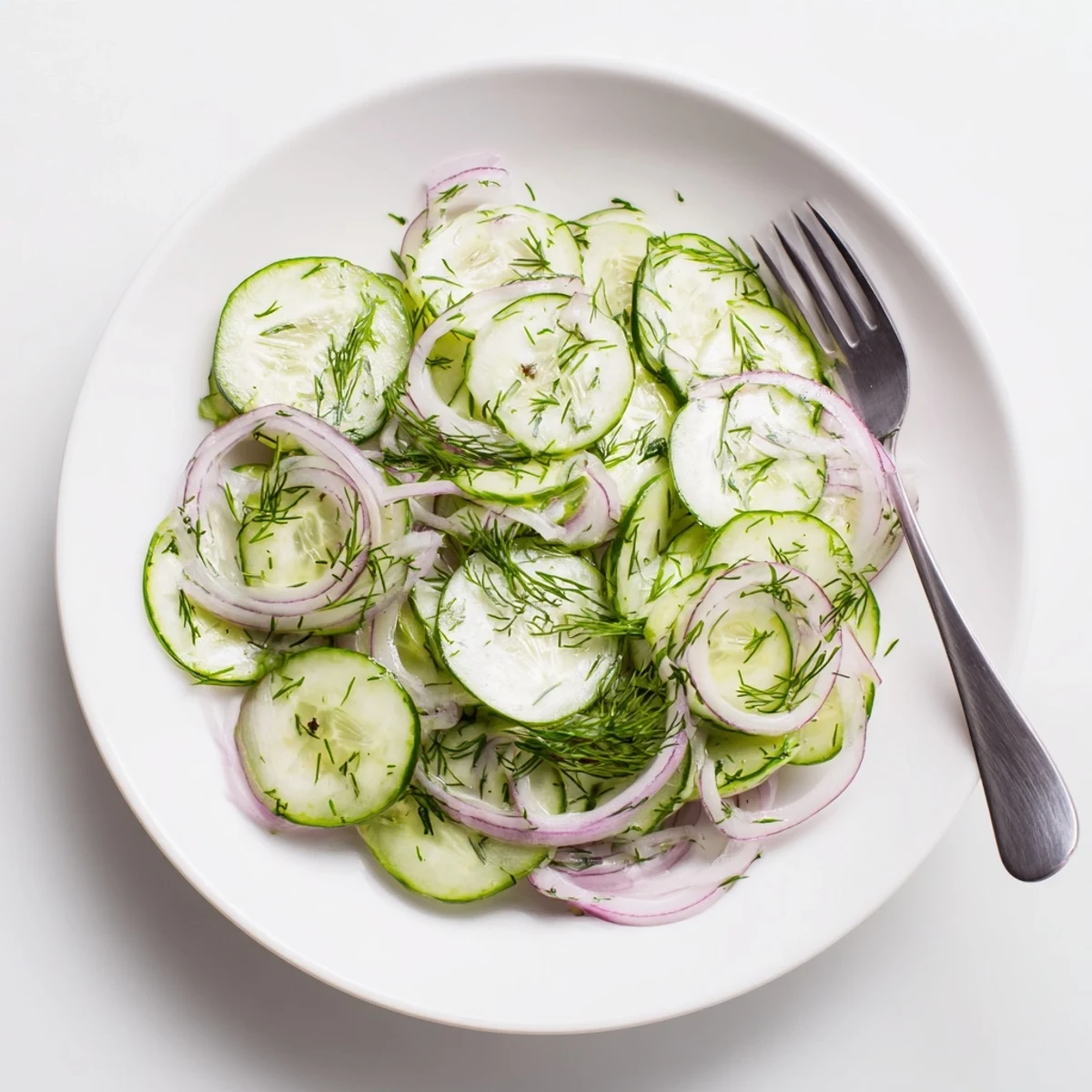 Glass serving dish of refreshing cucumber salad featuring crisp vegetables coated in sweet tangy dressing