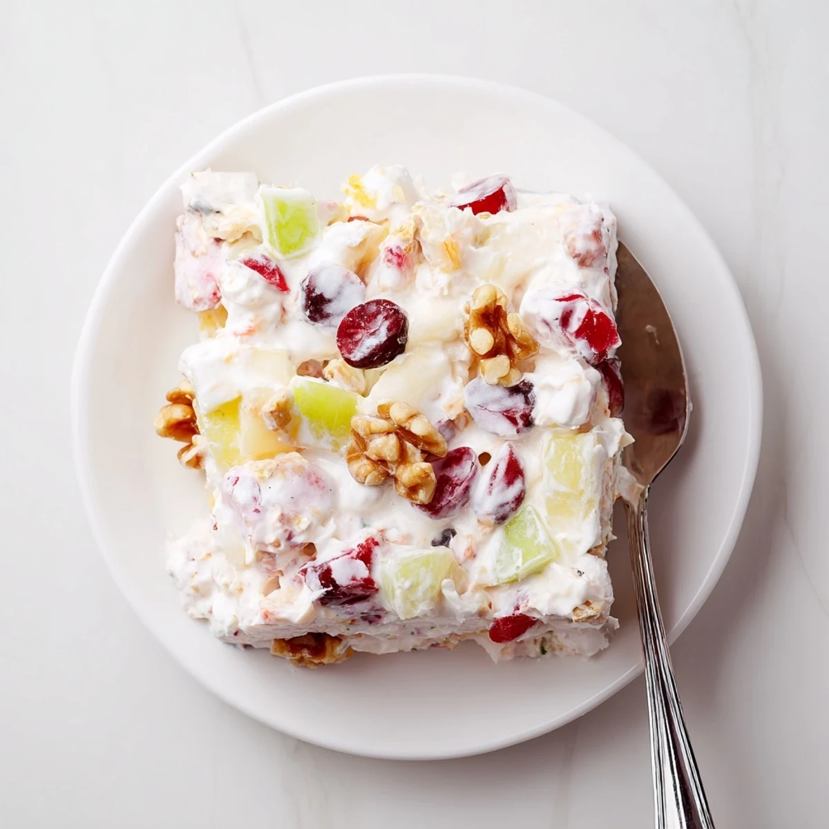Sliced square of frozen cranberry salad featuring red berries, green grapes, and walnuts in creamy white filling