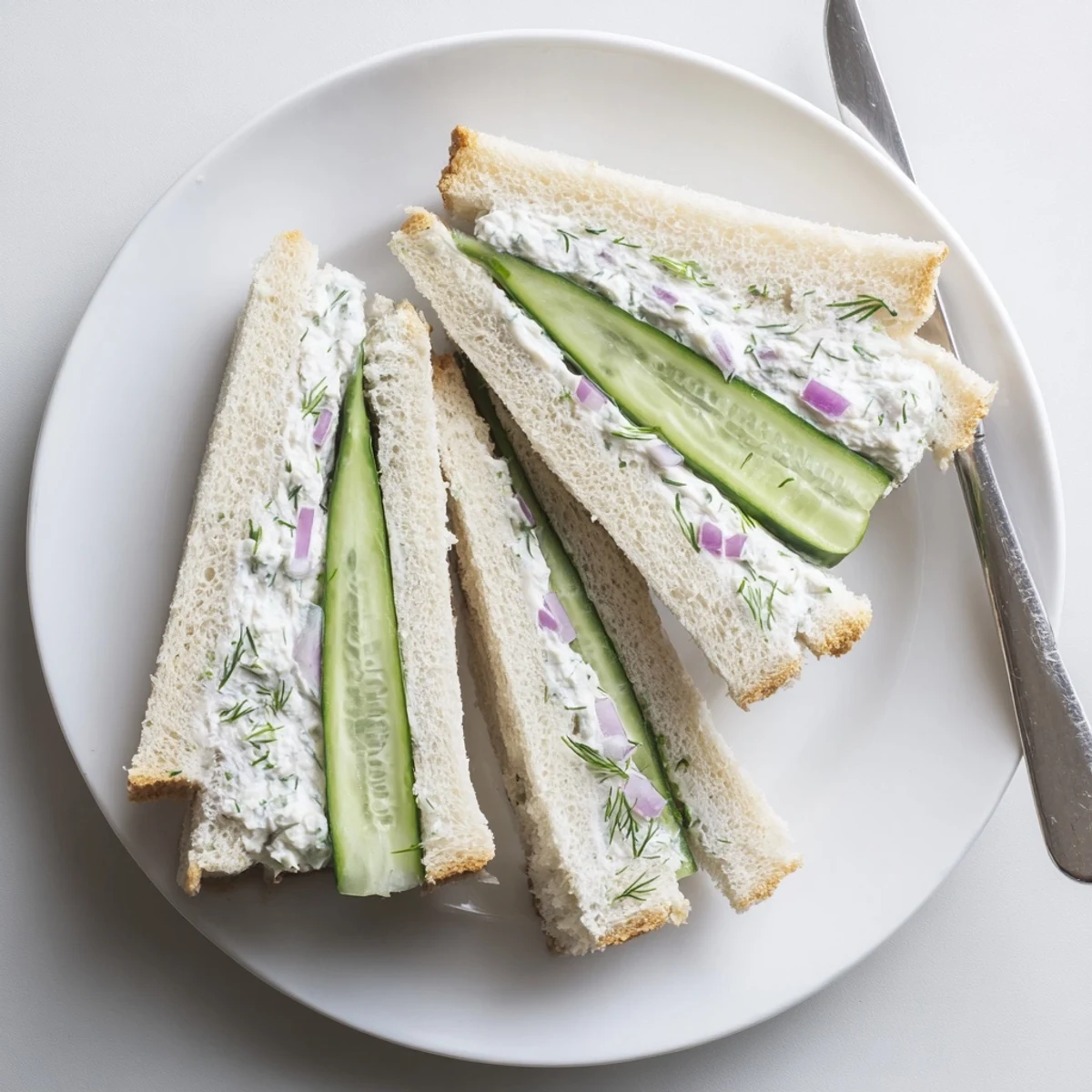 Tea-style cucumber salad sandwiches with creamy herbed cheese spread on soft white bread triangles
