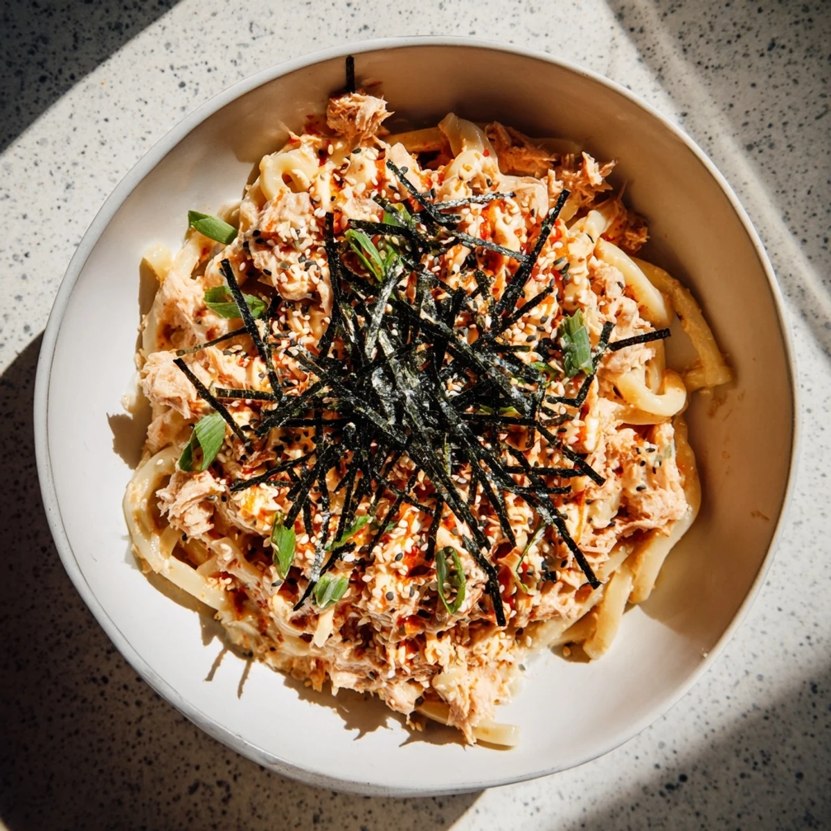 Spicy tuna udon noodles in a bowl topped with scallions and sesame seeds