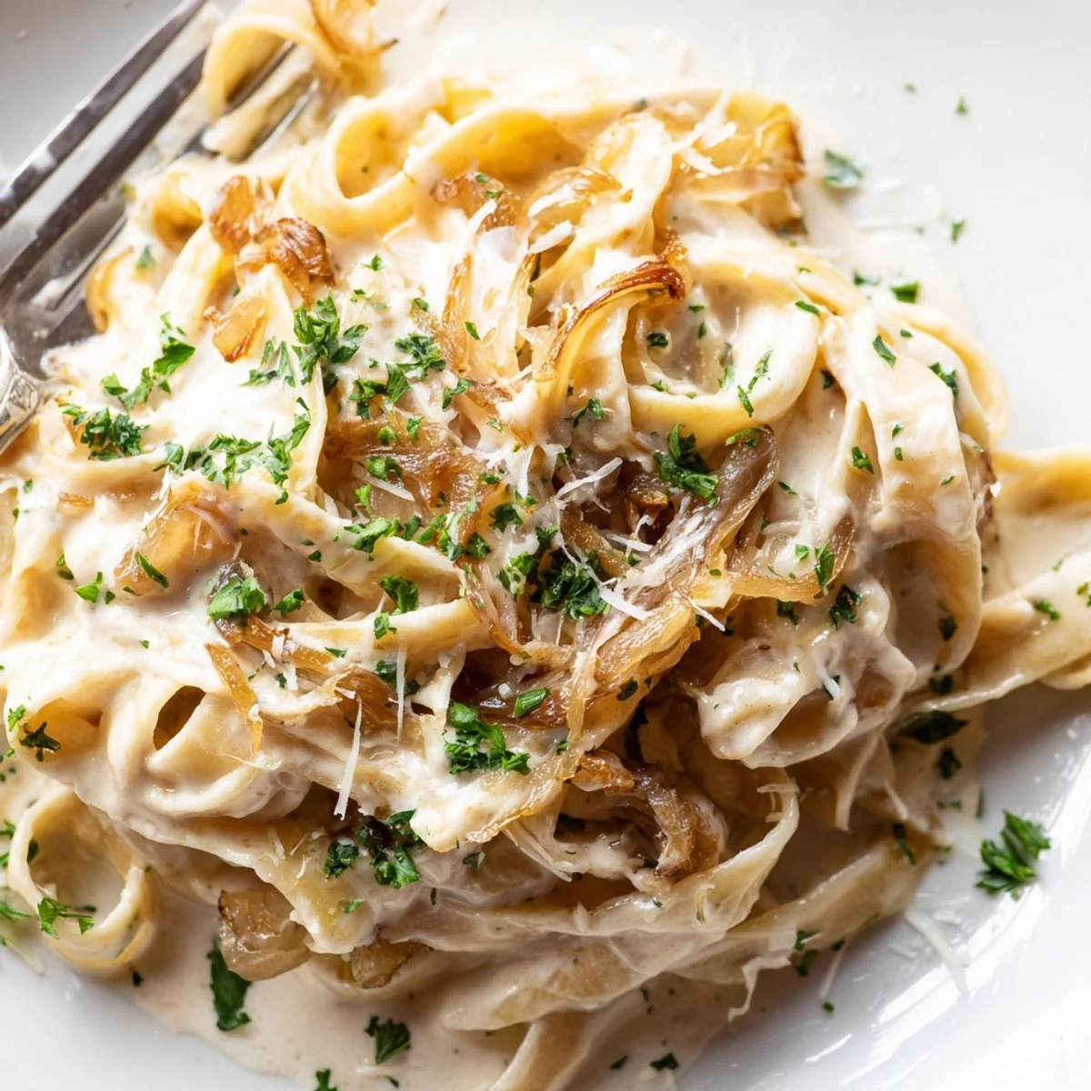 Creamy caramelized onion pasta dish garnished with fresh parsley and extra Parmesan cheese on a white plate