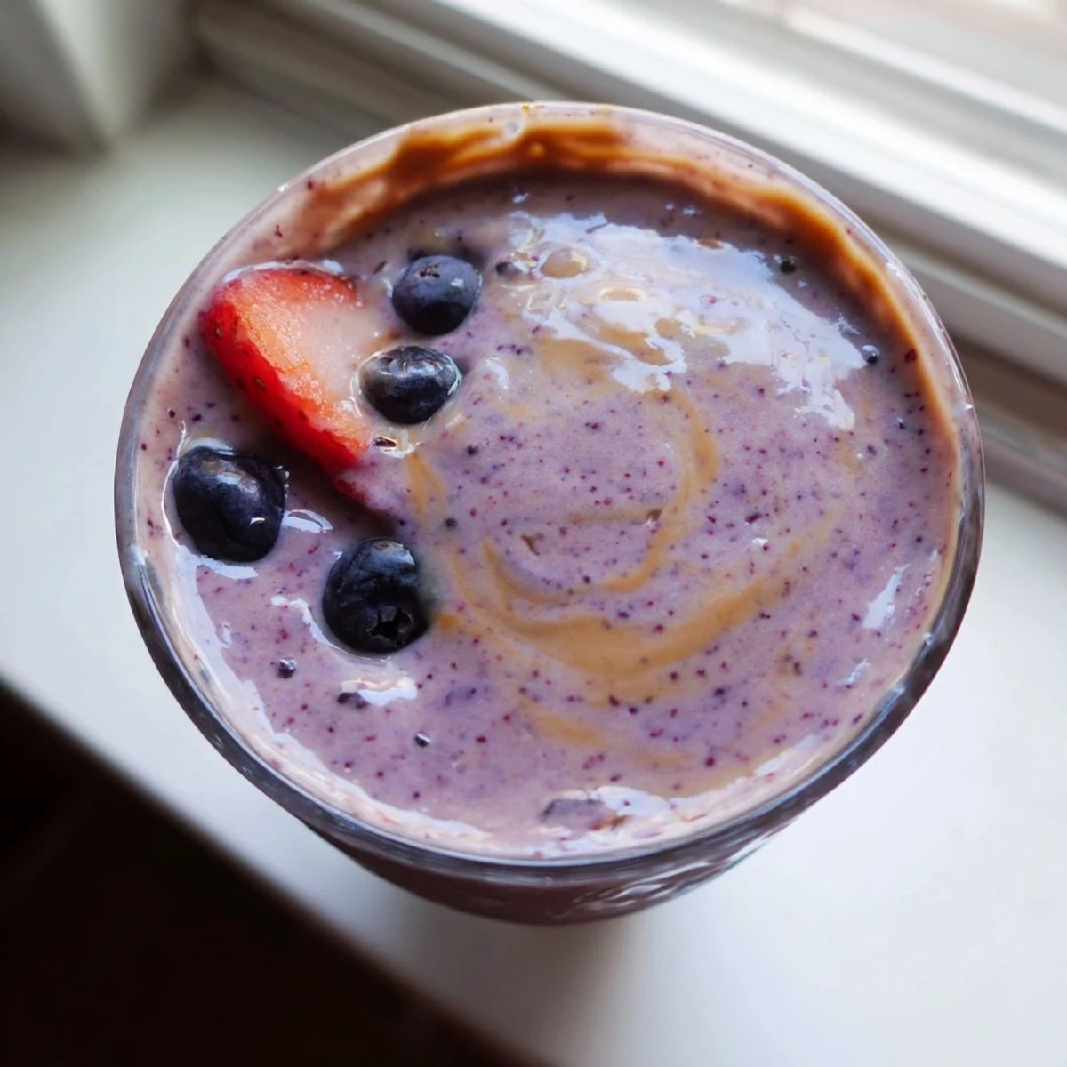 Thick purple peanut butter berry smoothie topped with fresh strawberries in a glass jar