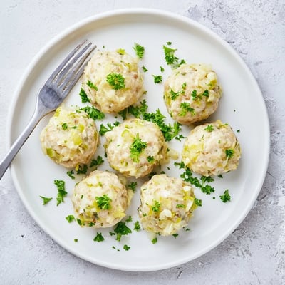 Freshly cooked German Cabbage Dumplings in a white bowl garnished with parsley, ready to serve with a creamy mushroom sauce for a hearty meal.