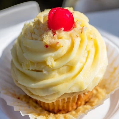 Moist pineapple-infused Dole Whip Cupcakes piped with creamy yellow frosting on a plate